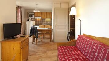 Un espace de vie compact comprenant un coin cuisine, une table à manger en bois, un canapé et un téléviseur posé sur un meuble en bois.