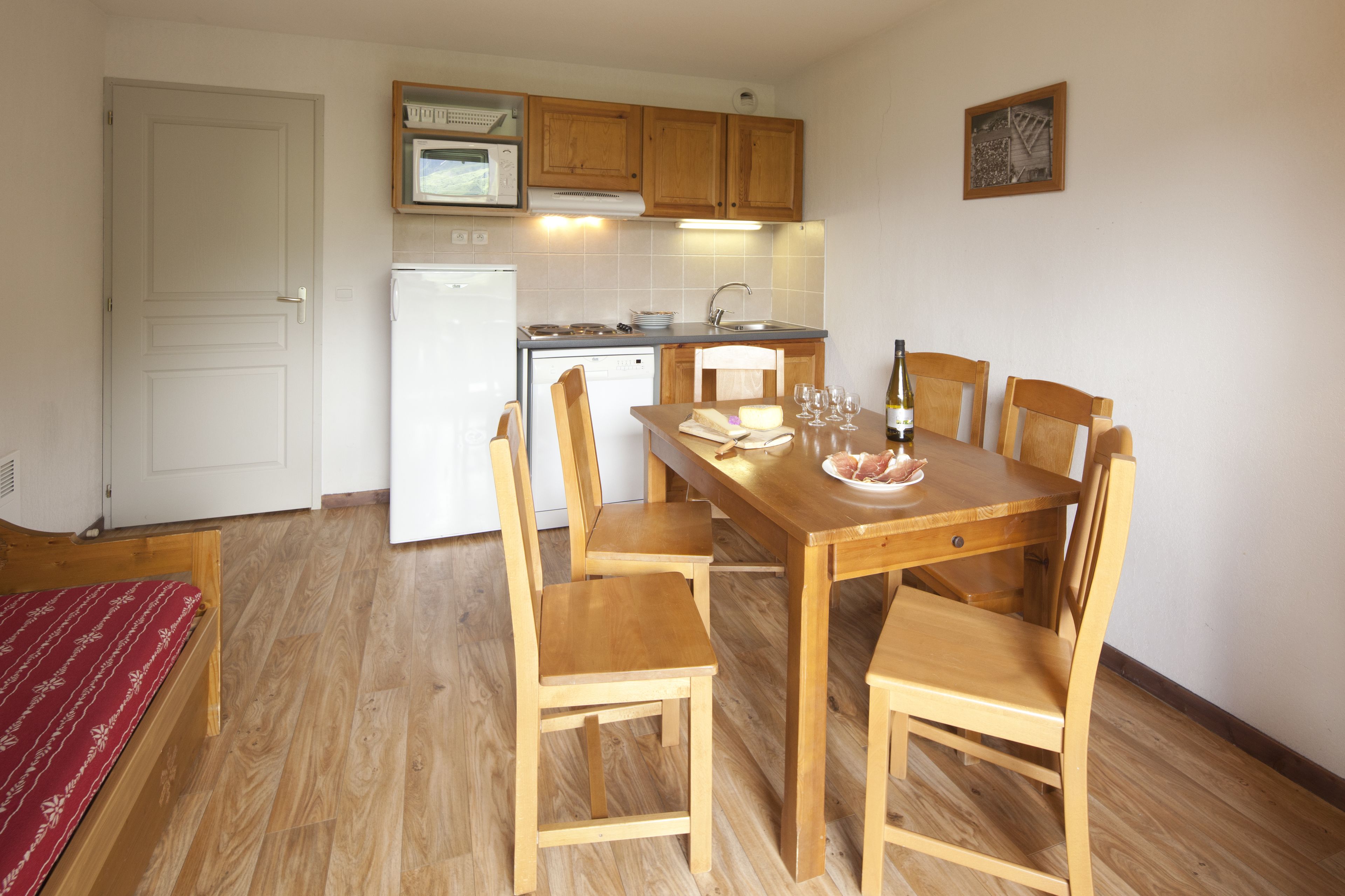 Een compacte keuken met houten kastjes, een witte koelkast en een eettafel met stoelen.