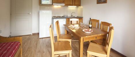 Een compacte keuken met houten kastjes, een witte koelkast en een eettafel met stoelen.