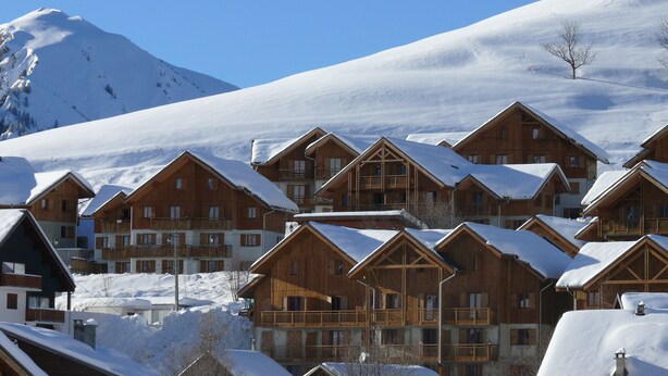 Un conjunto de edificios de estilo chalé, con balcones, frente a una montaña cubierta de nieve.