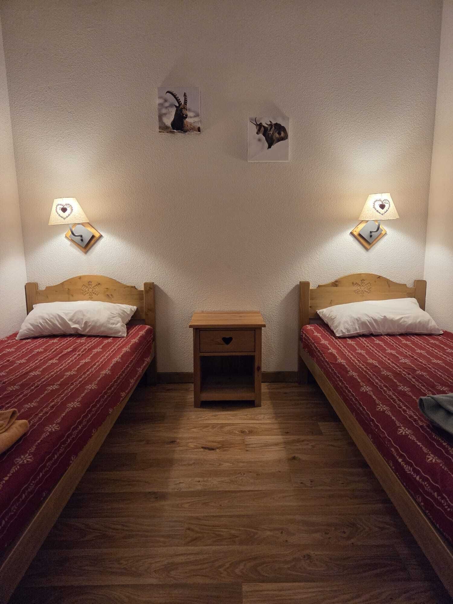 Une petite pièce avec deux lits simples, une table de chevet en bois et deux lampes fixées au mur.