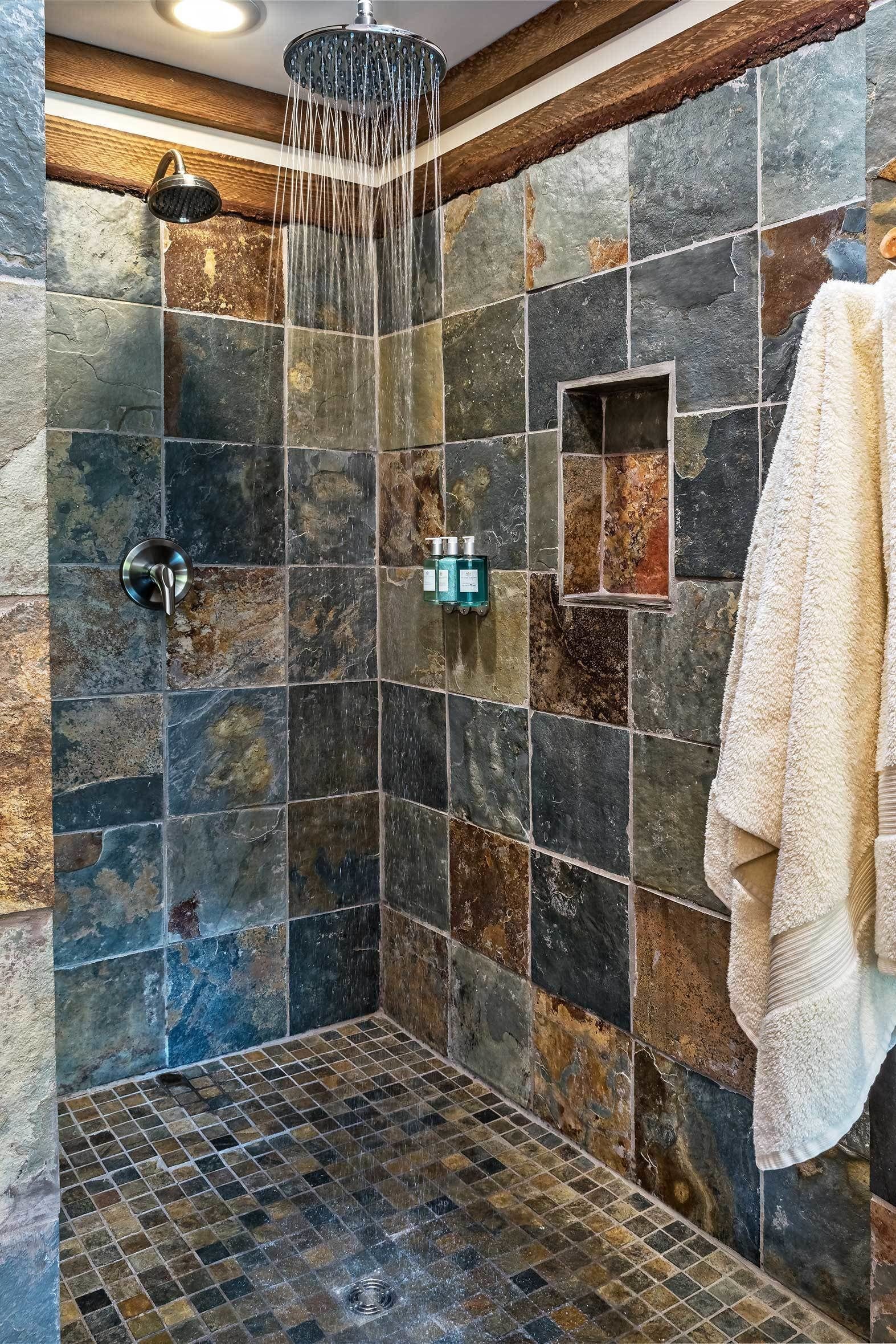 A shower with a rain showerhead, stone tiles, and a towel hanging on the wall.