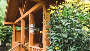 A wooden porch with a hanging lantern and a large bush of yellow flowers. - Carson Ridge Luxury Cabins (Carson)