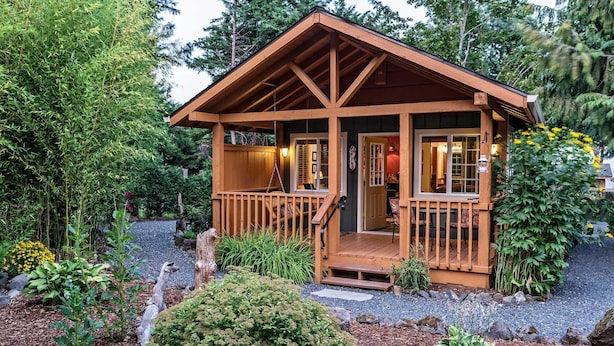 A wooden cabin with a porch, surrounded by a garden with various plants and a gravel path. - Carson Ridge Luxury Cabins (Carson)