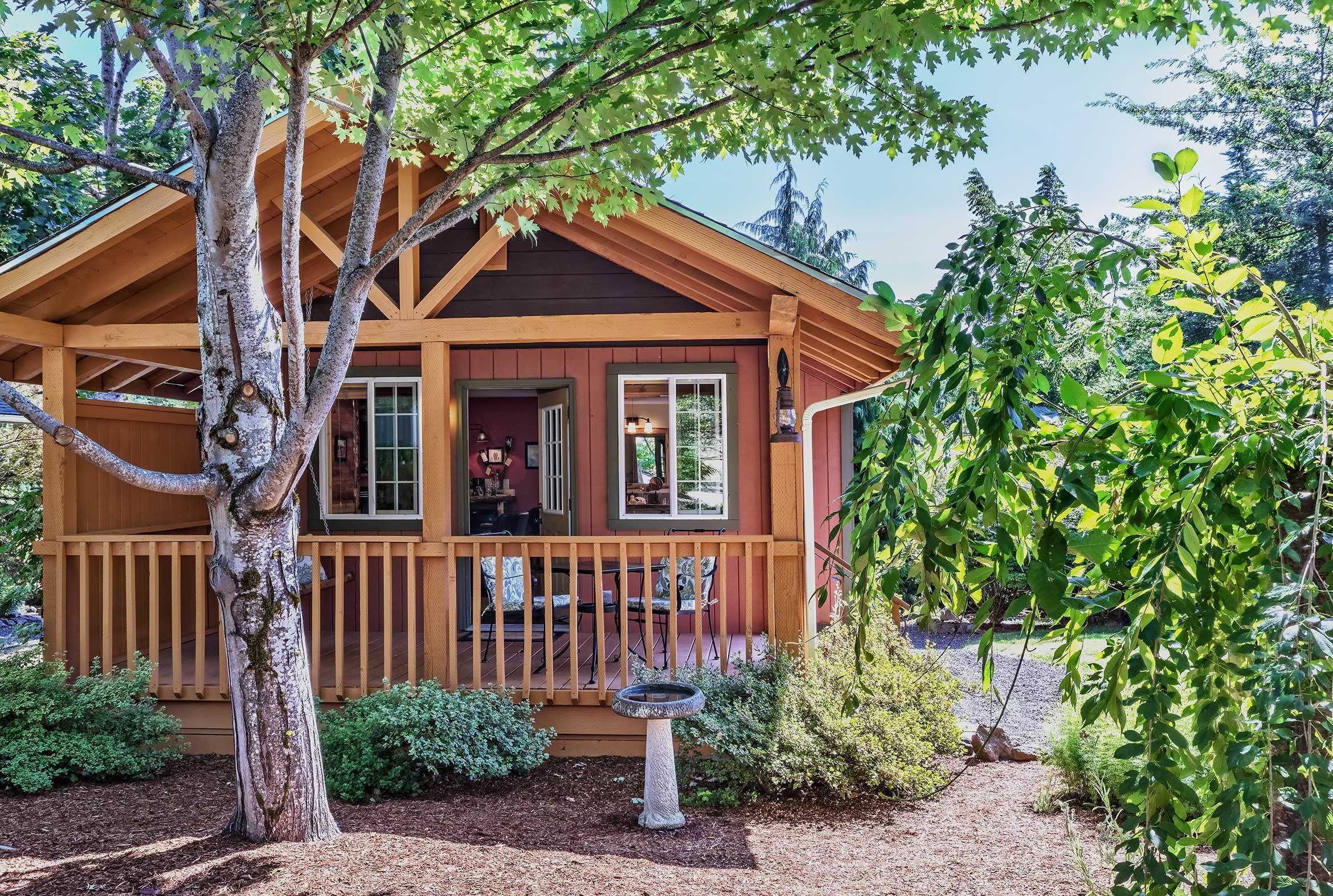 A wooden cabin with a porch, surrounded by trees and shrubs.