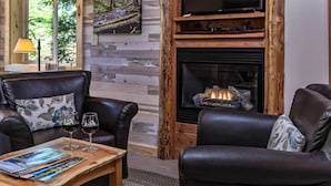 A cozy living room with a fireplace, leather sofas, and a coffee table with magazines and glasses. - Carson Ridge Luxury Cabins (Carson)