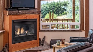 A cozy living room with a fireplace, leather sofa, and a view of a deck with a wooden railing. - Carson Ridge Luxury Cabins (Carson)