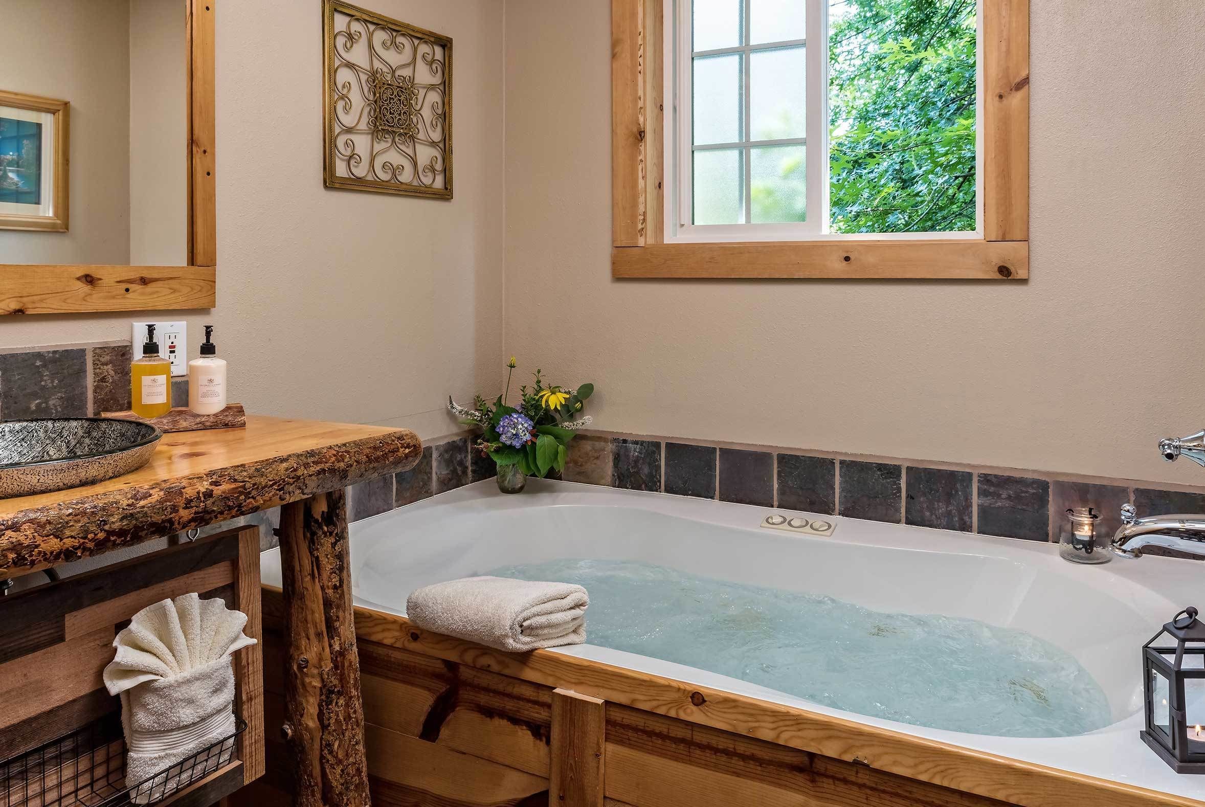 A bathroom with a wooden vanity, a bathtub, and a window with a view of greenery.