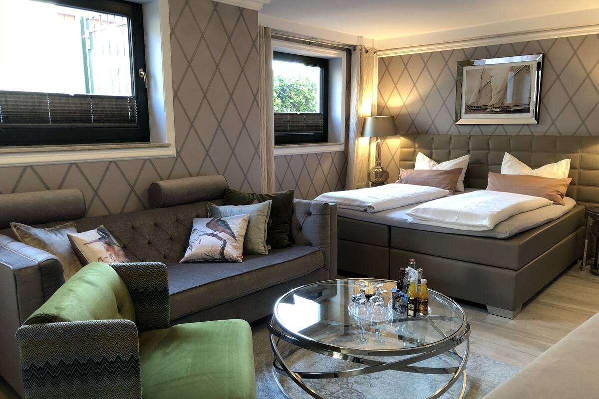 A modern bedroom with a sofa, a glass coffee table, a bed with pillows, and a nightstand.