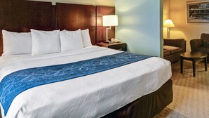A hotel room with a large bed, a nightstand with a lamp, a chair, and a small table. - Comfort Suites near Hot Springs Park (Hot Springs)