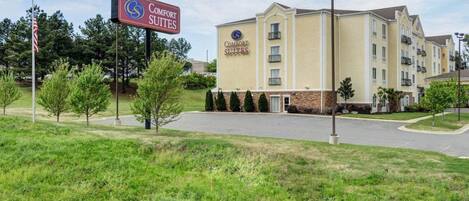 A Comfort Suites hotel with a two-story building, a parking lot, and a grassy area with trees.