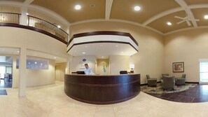 Zona de recepción de un hotel con un mostrador curvo, una recepcionista y un área de descanso con sillas.