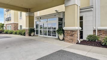 Enter a serene hotel with a covered walkway leading to a glass door entrance, surrounded by lush greenery and stone accents.