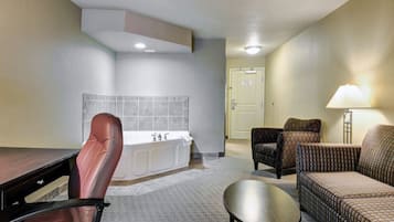 Habitación de hotel con escritorio, silla de oficina, dos sillones, un sofá, una mesita y un baño con bañera y lavamanos.