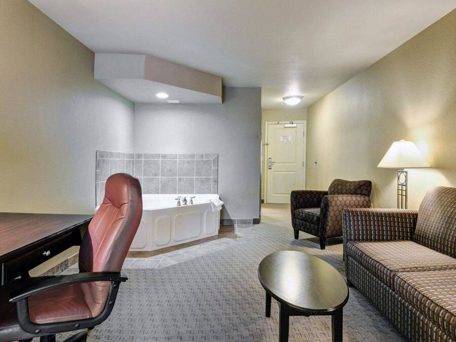Habitación de hotel con escritorio, silla de oficina, dos sillones, un sofá, una mesita y un baño con bañera y lavamanos.