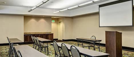 A conference room with long tables and chairs, a projector screen, and a podium.