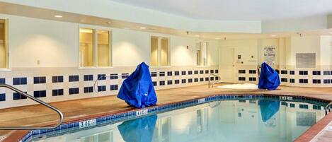 Une piscine intérieure avec un bord carrelé, une rampe métallique et deux bâches bleues pour recouvrir la piscine.