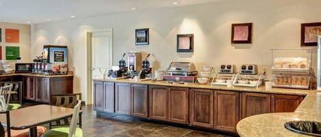 A hotel kitchen with a buffet setup, including a coffee station, a microwave, and a display case with pastries.