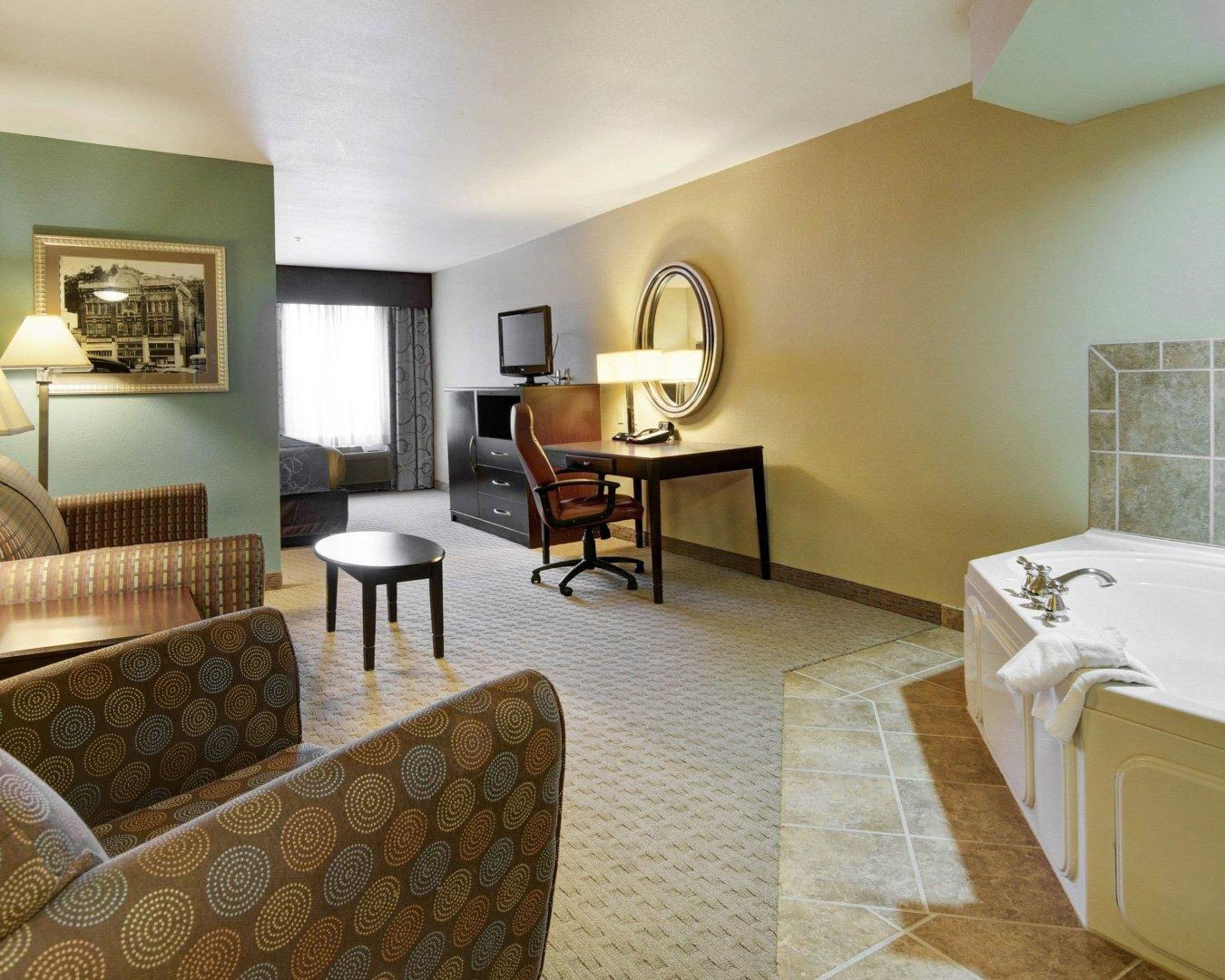A hotel room with a bed, a desk with a chair, a sofa, a small table, a TV, and a mirror.