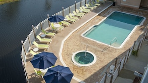 Un área de piscina con sillas de descanso y sombrillas, una piscina pequeña y circular, y una piscina rectangular.