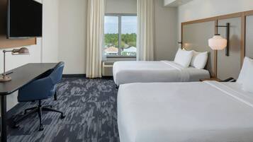 A hotel room with two beds, a desk, a chair, a television, and a window with curtains.