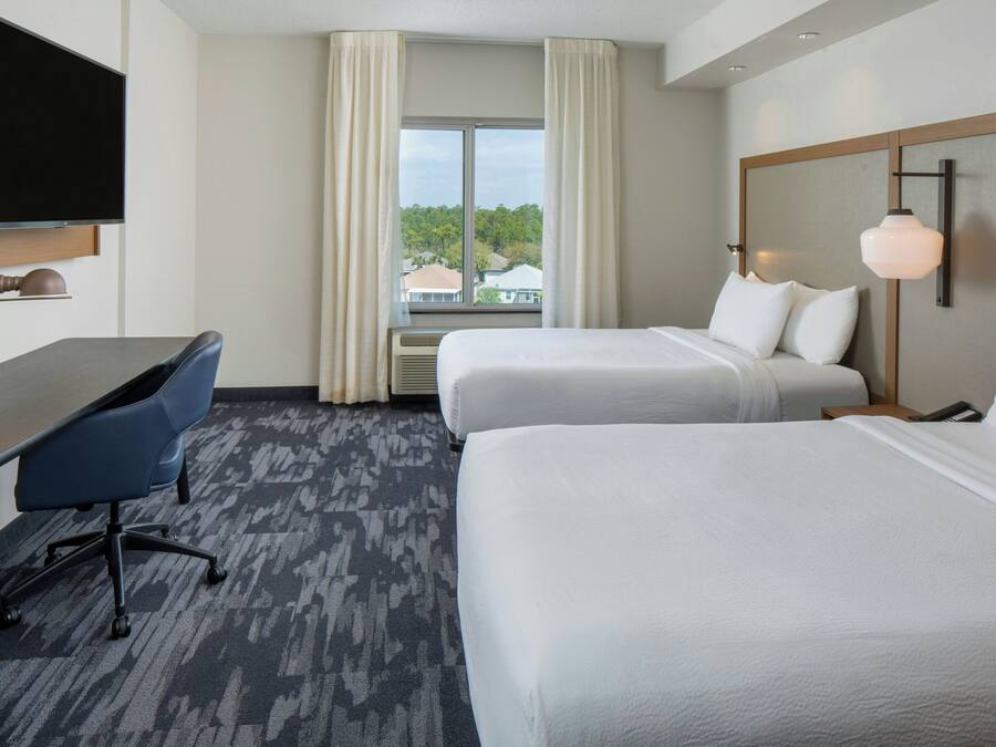 A hotel room with two beds, a desk, a chair, a television, and a window with curtains.