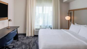 A hotel room with a bed, desk, chair, TV, and window with curtains.