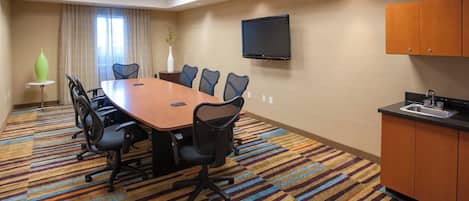 Un salón de conferencias con una gran mesa, sillas, un televisor y una kitchenette.