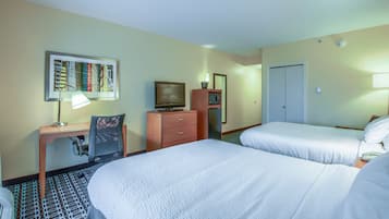 Une chambre d’hôtel avec deux lits, un bureau avec une lampe, une chaise, une commode, un téléviseur et un four à micro-ondes.