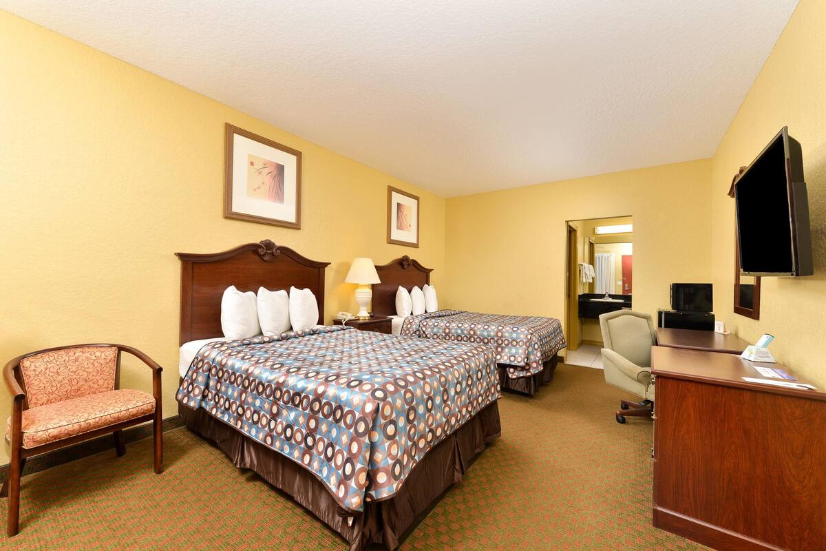 A hotel room with two beds, a desk, a chair, and a television.