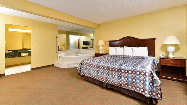 A hotel room with a bed, bedside lamps, a nightstand, a mirror, a bathroom with a sink and a bathtub.