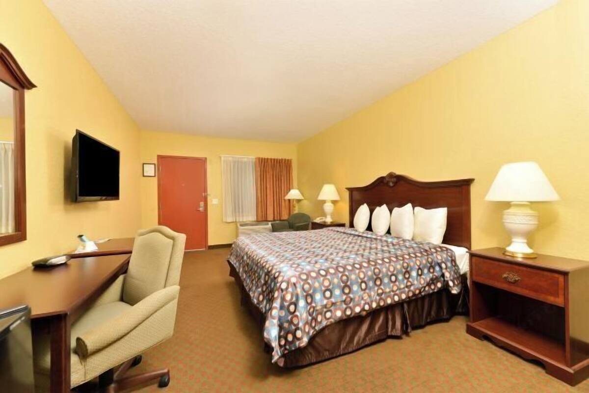 A hotel room with a bed, desk, chair, TV, and lamps.