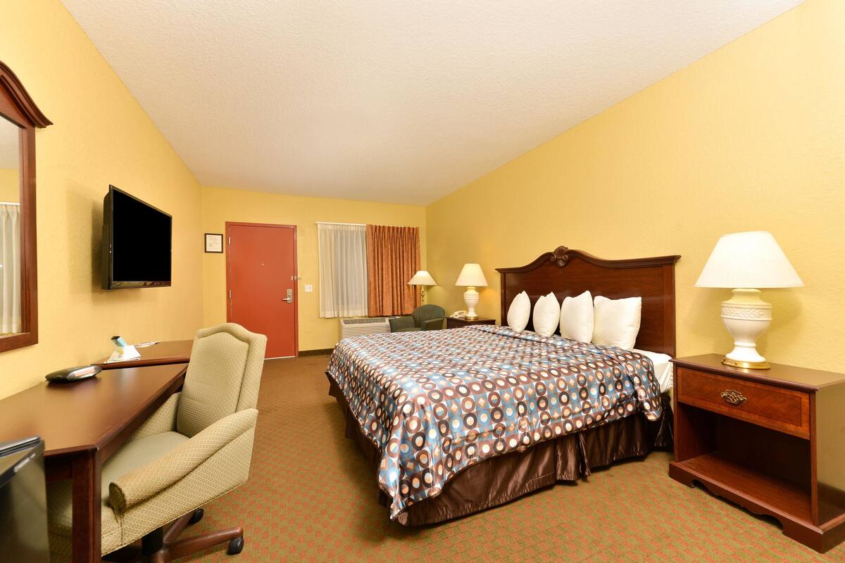 A hotel room with a bed, a desk, a chair, a TV, and a lamp.