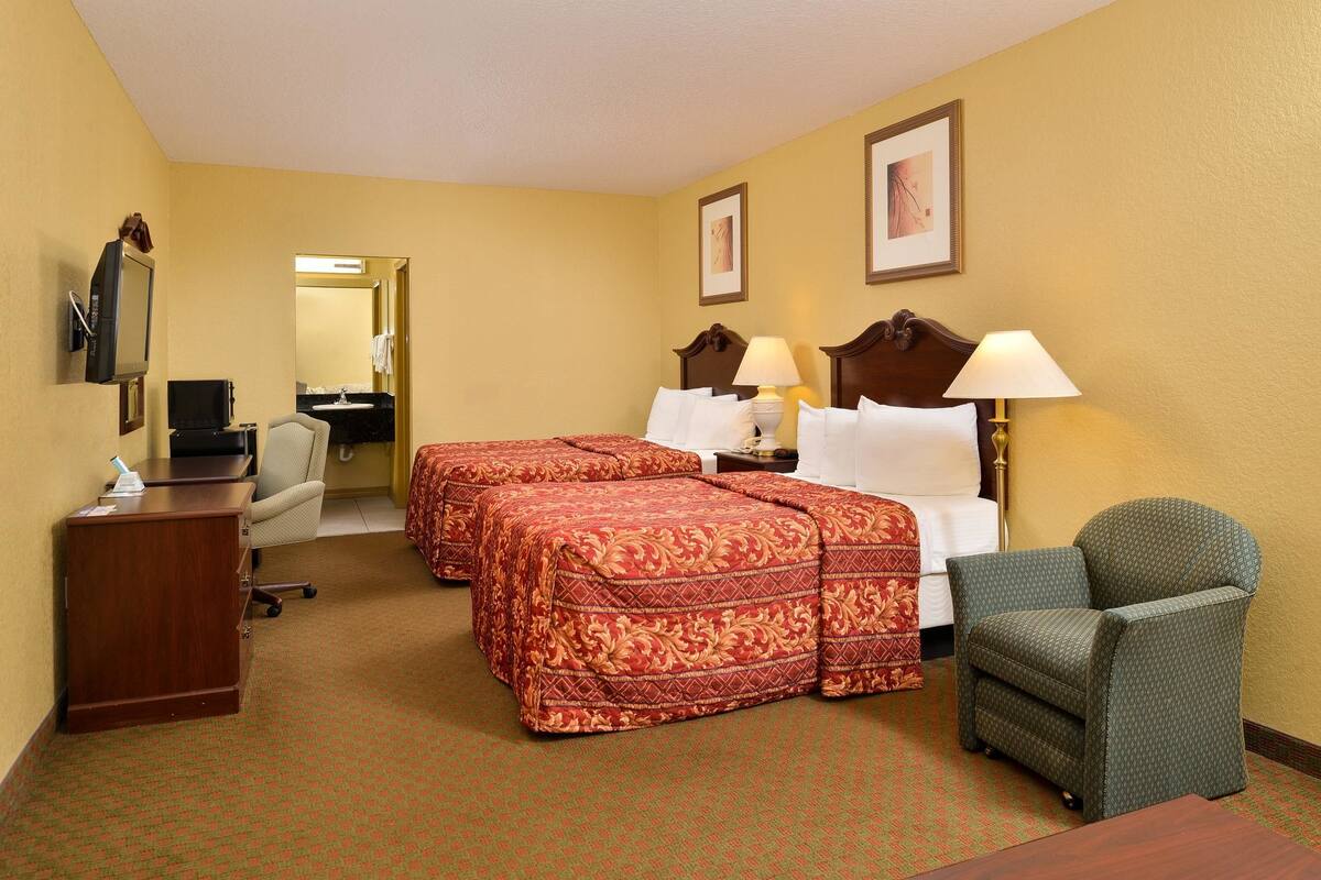 A hotel room with two beds, a desk, a chair, and a TV.