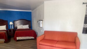 A hotel room with two beds, a red couch, wooden flooring, and a wall with a blue accent.