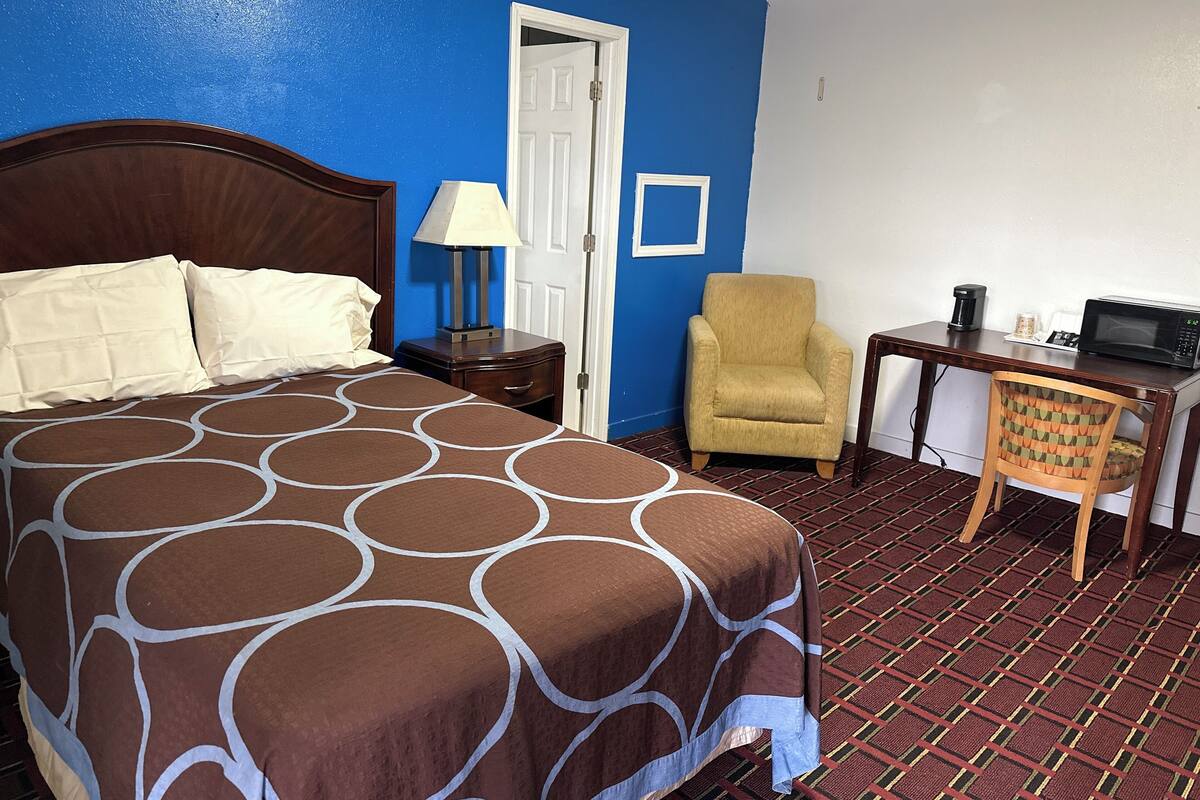 A hotel room with a bed, a chair, a desk with a computer, and a coffee maker.