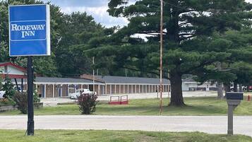 A motel named Rodeway Inn with a large tree in the foreground and a building with a red roof in the background.