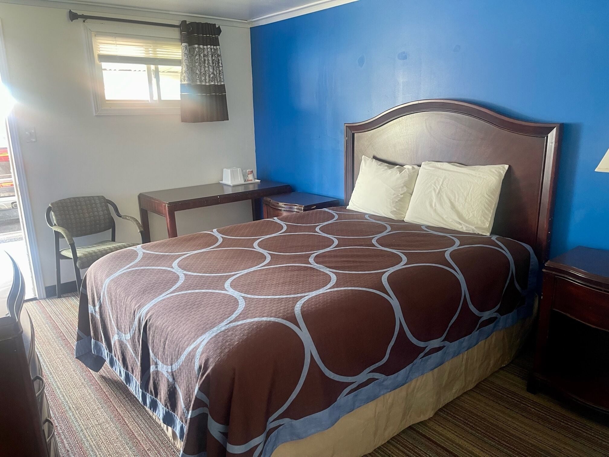 Quarto de hotel com cama, escrivaninha, cadeira e janela com cortinas.