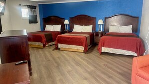 A hotel room with three beds, wooden headboards, and a wooden floor.