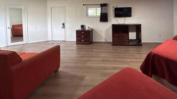 A room with two red sofas, a wooden dresser, a television on the wall, and a door leading to another room.