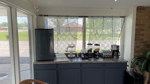 A kitchen with a refrigerator, coffee maker, toaster, and a window with curtains.