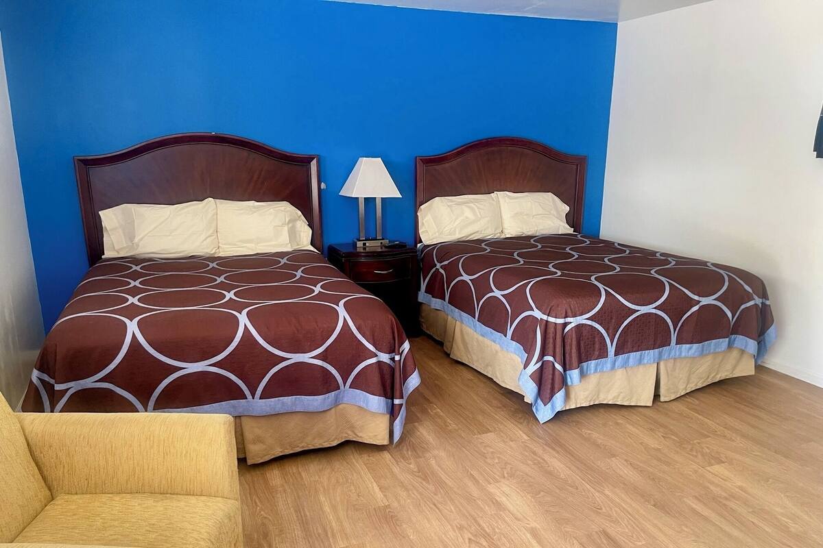 A room with two beds, a nightstand, a lamp, and a wooden floor.