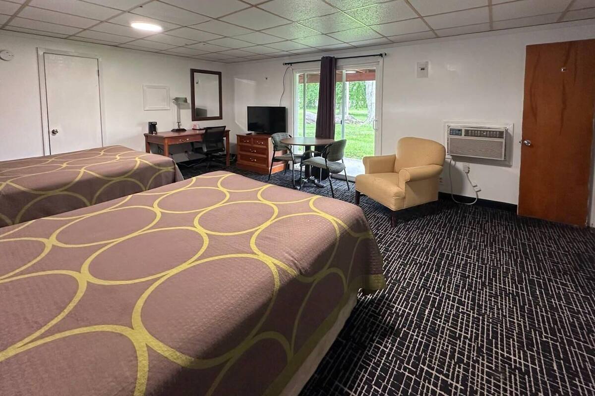 A hotel room with two beds, a desk, a chair, a television, and a window with a view of greenery.