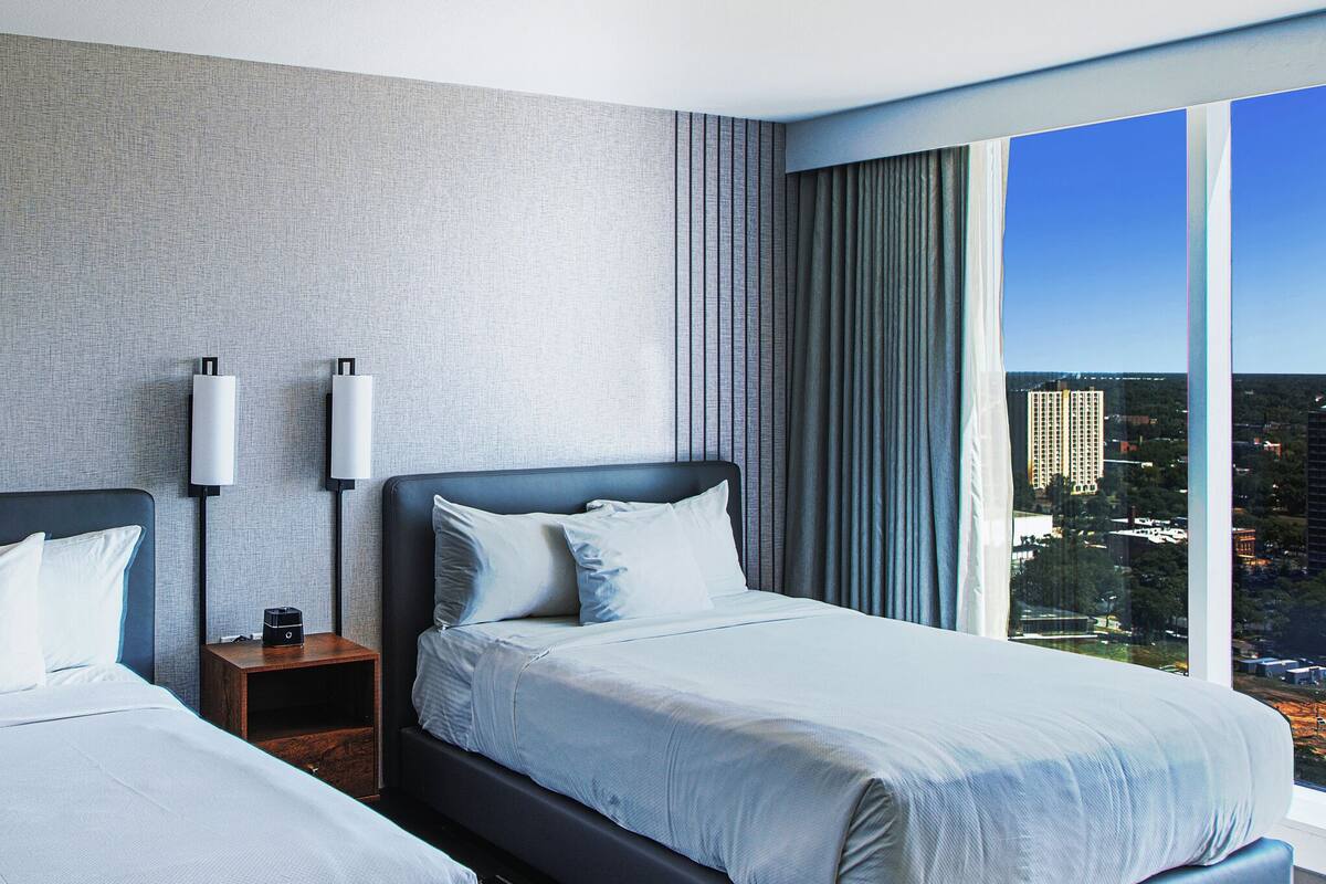 Ein Hotelzimmer mit zwei Betten, einem gerahmten Bild an der Wand und Blick auf die Stadt durch das Fenster.