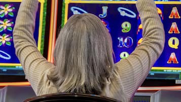 A person seated at a slot machine, with their hands raised in anticipation.