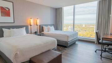 Habitación de hotel con dos camas, un escritorio y una silla. Amplia ventana con vistas a la ciudad.