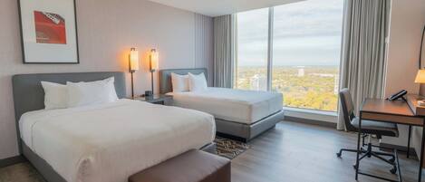 Habitación de hotel con dos camas, un escritorio y una silla. Amplia ventana con vistas a la ciudad.