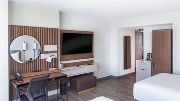 A hotel room with a bed, a desk with a chair, a television, a mirror, and a wardrobe.
