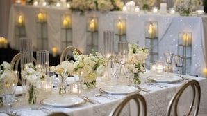 A table set for a formal event with white tablecloths, clear glass candle holders, and white flowers.