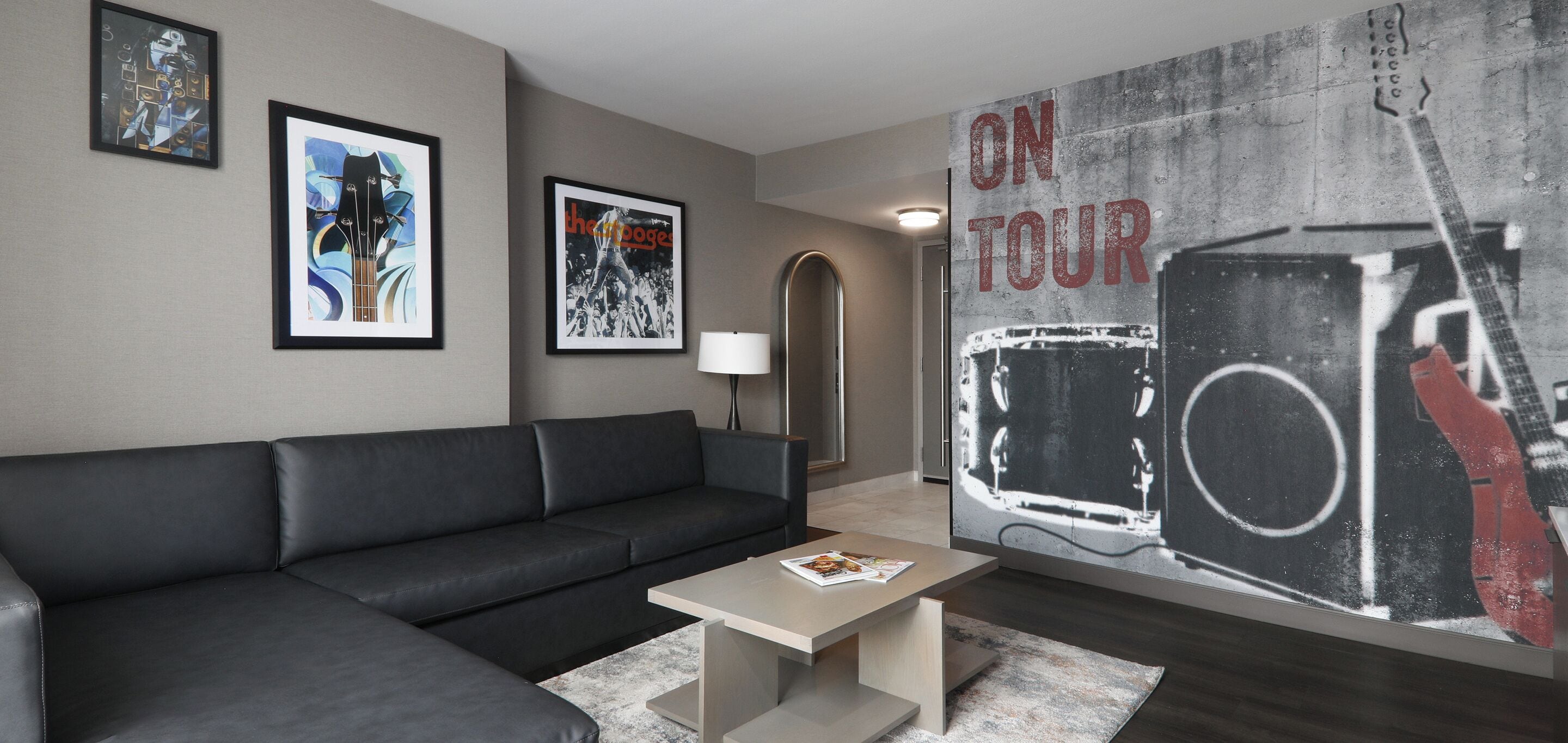 Un salon moderne avec un canapé en cuir noir, une table basse, des œuvres d’art encadrées accrochées aux murs et une grande affiche sur le mur.